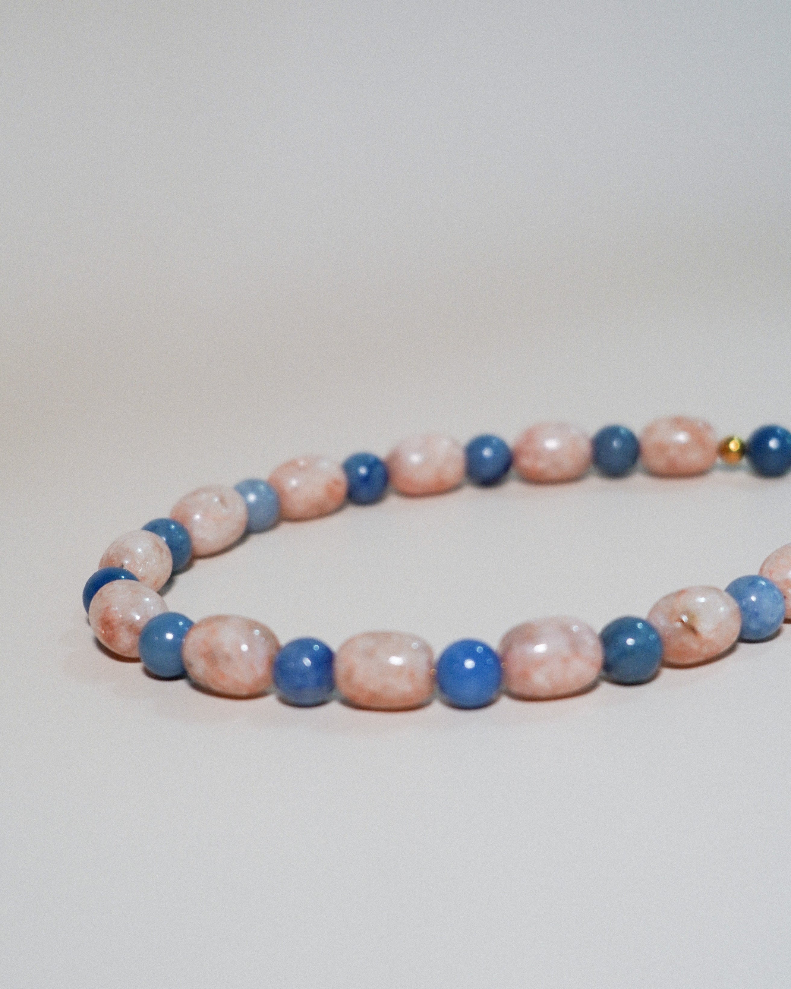 A beaded strand necklace or bracelet made of alternating pink and blue marbled beads, photographed on a plain light background.