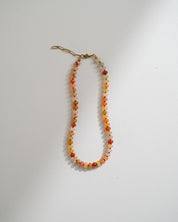A beaded necklace with small round beads in orange, red, yellow, and white, featuring a gold-toned lobster clasp, displayed on a plain white surface.